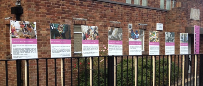 Exhibition of boards tied to railings with photos and text about projects 